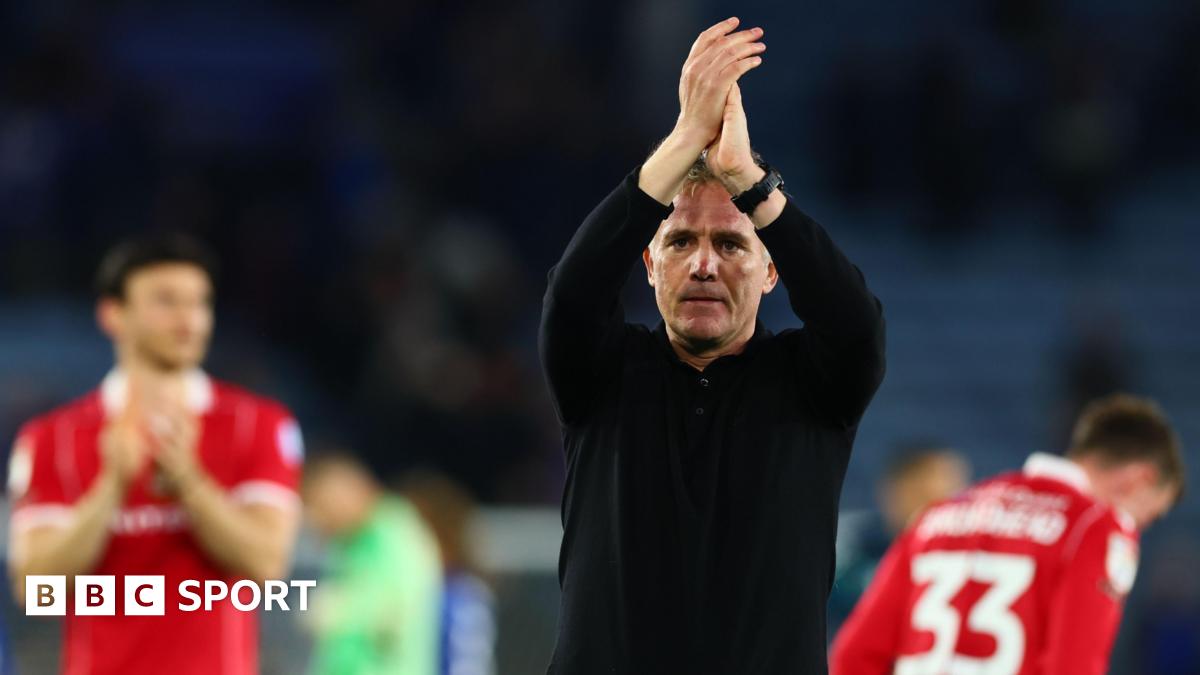 Manager Phil Parkinson, dressed in a black top and trousers, applauds supporters with Wrexham players behind him in the background