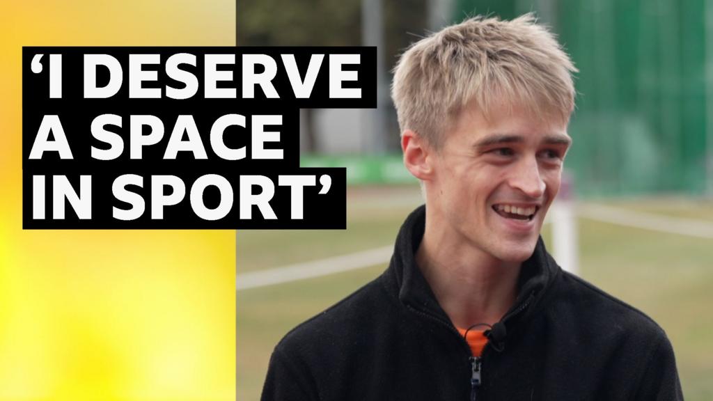 Athlete Seamus Derbyshire smiling whilst sitting down at an athletics track. He is wearing a black jumper. The words next to him are: 