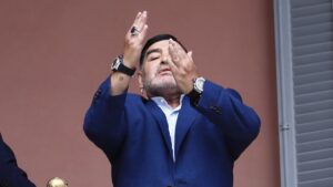 Diego Maradona gestures to fans next to a small, generic replica of a FIFA World Cup soccer trophy at the Casa Rosada government house after his meeting with Argentine President Alberto Fernandez, Buenos Aires, Argentina, Dec. 26, 2019. (AP Photo)